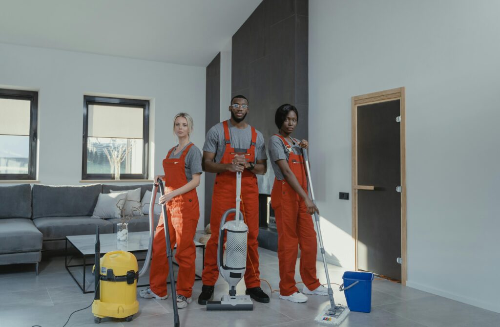 pexels-photo-6195125-6195125 Diverse cleaning team in red uniforms ready to sanitize a modern living room with vacuum and mop.